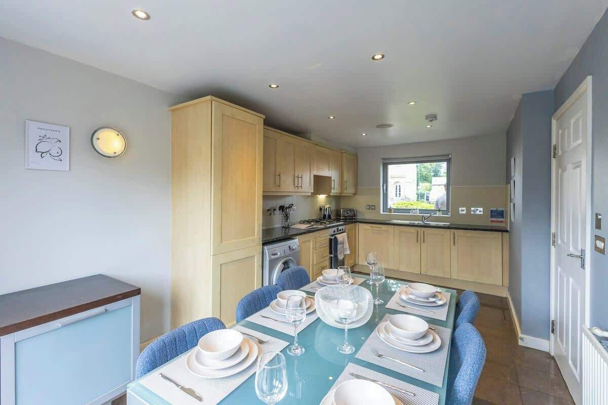 A modern kitchen with wooden cabinets, a dining table set for four, and a view of the outdoors.