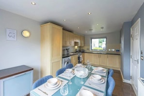 A modern kitchen with wooden cabinets, a dining table set for four, and a view of the outdoors.