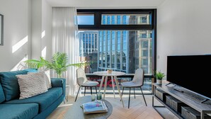 Un salon moderne comprenant un canapé, une table basse et un meuble pour la télévision, avec une grande fenêtre offrant une vue sur la ville.