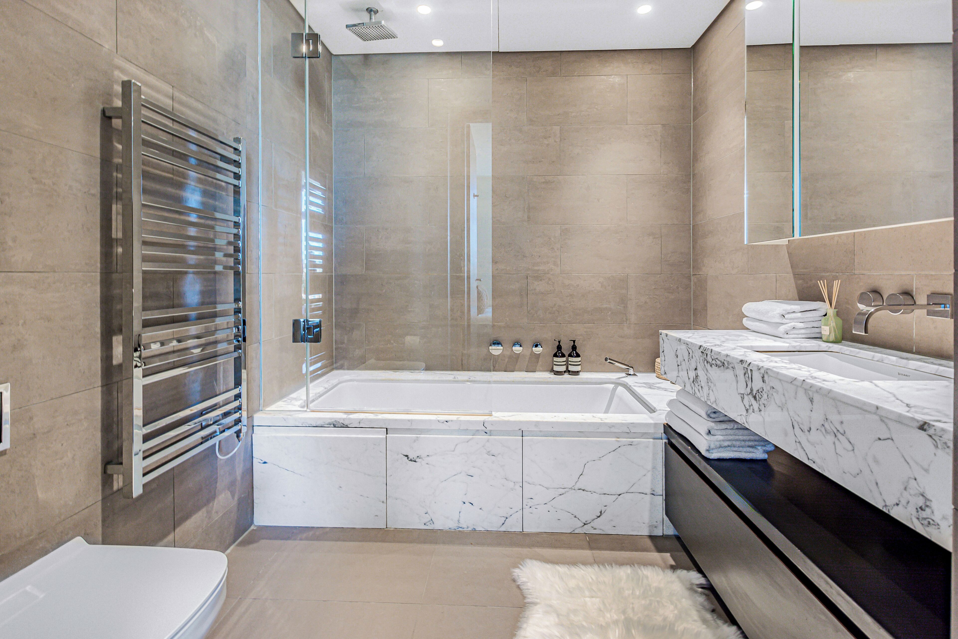 A modern bathroom with a bathtub, a glass-enclosed shower, and a marble vanity.