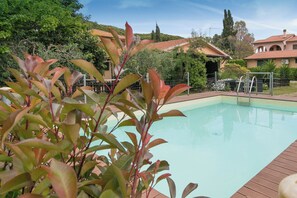 A swimming pool surrounded by greenery and a building with a tiled roof.