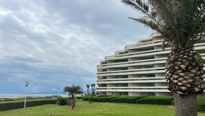 A multi-story hotel with balconies, a grassy lawn, palm trees, and a beach in the background. - CANET SUD PANORAMIC SEA VIEW EXCEPTIONAL APARTMENT (Canet-en-Roussillon)