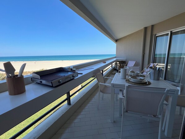 A balcony with a grill, dining table, and chairs overlooking a beach. - CANET SUD PANORAMIC SEA VIEW EXCEPTIONAL APARTMENT (Canet-en-Roussillon)