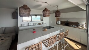 A modern kitchen with a central island, wicker pendant lights, and a view of the sea. - CANET SUD PANORAMIC SEA VIEW EXCEPTIONAL APARTMENT (Canet-en-Roussillon)