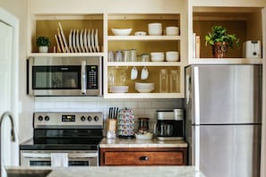 A kitchen with stainless steel appliances, including a microwave, oven, and refrigerator, with white cabinets and a tiled backsplash.