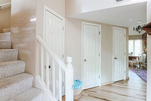 A staircase with white railings leading to a door, a hallway with wooden flooring, and a dining area in the background.