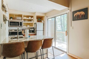 A modern kitchen with a central island, bar stools, and a sliding glass door leading to a deck.