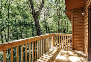 A wooden deck with a railing overlooking a forested area.