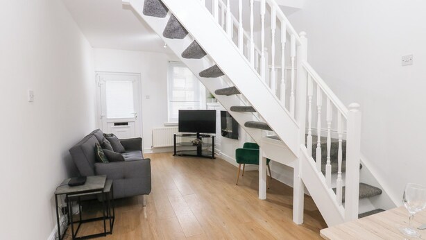 A modern living room with a staircase, a grey sofa, a small table, and a TV. - Holly House (Whitehaven)