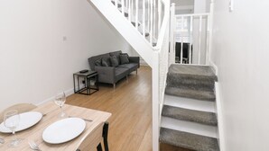 A modern living space with a staircase, a dining area with a table set for two, and a grey sofa. - Holly House (Whitehaven)