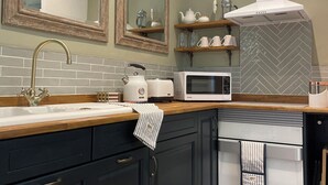 Et moderne køkken med vask, elkedel, brødrister, mikrobølgeovn og komfur. Der er skabe, et spejl og en backsplash med et fiskebensmønster.