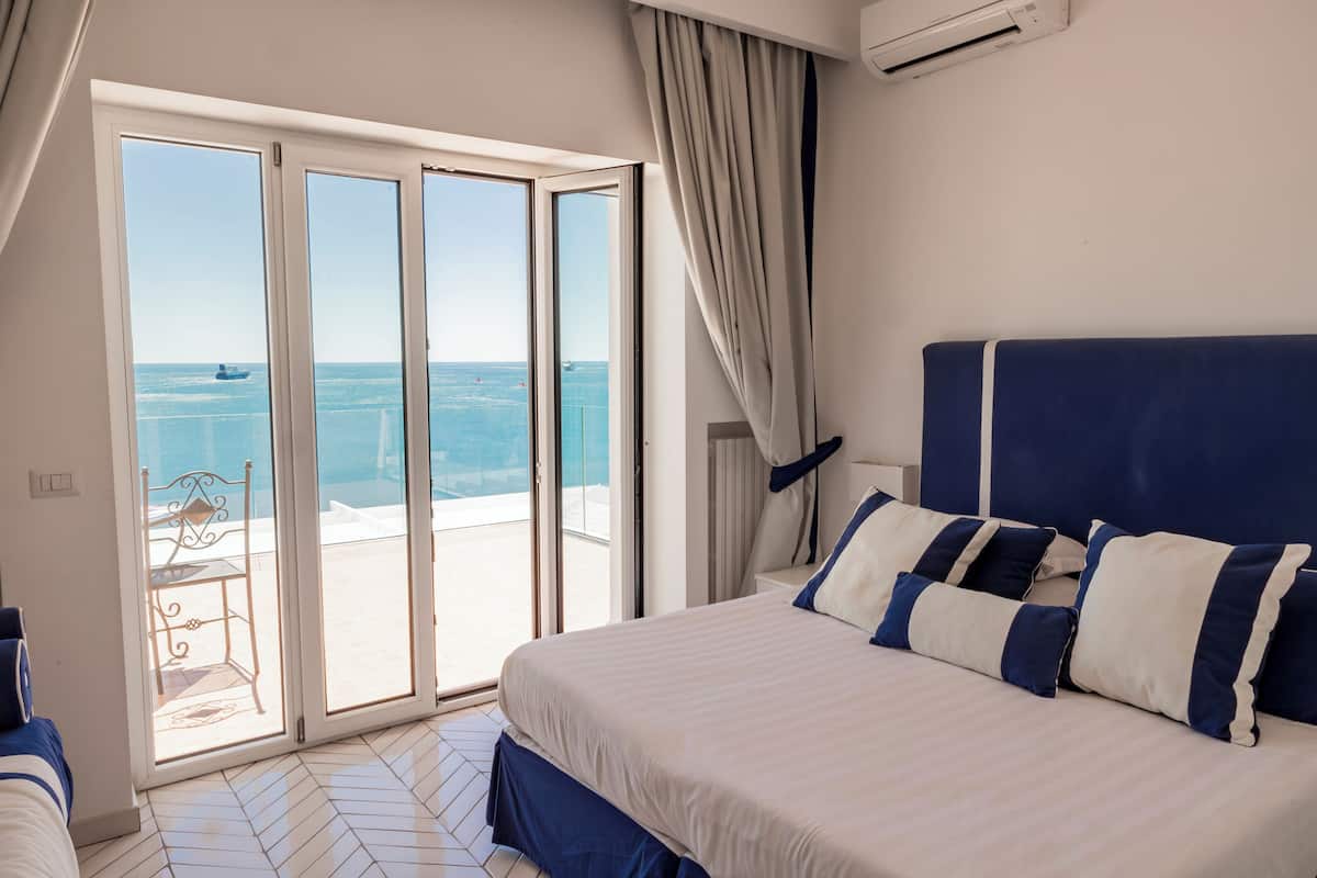 Une chambre avec un grand lit, une vue sur la mer par une porte coulissante et un balcon avec une chaise.