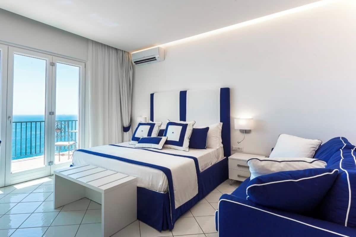 Une chambre d’hôtel comprenant un lit, une table de chevet, une chaise et un balcon avec vue sur la mer.