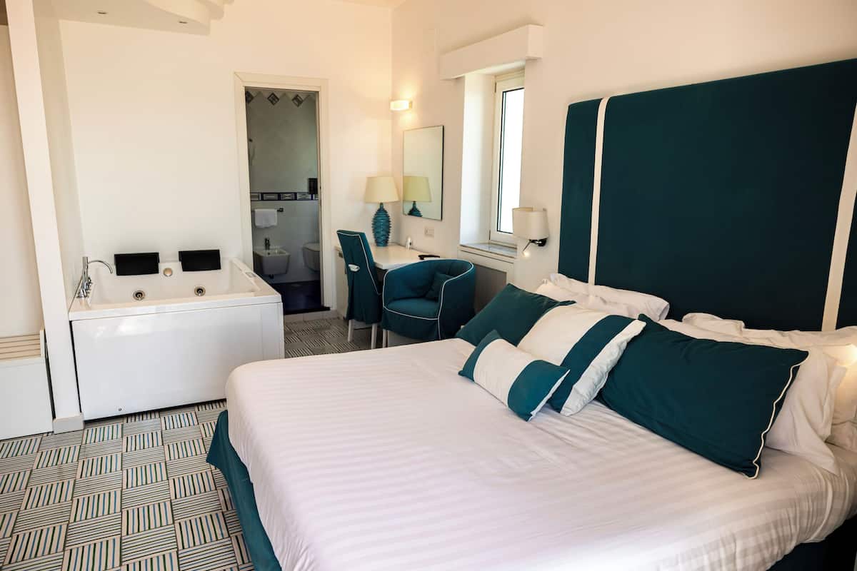 Une chambre d’hôtel avec un lit, un bureau, une chaise, une salle de bain et une fenêtre.
