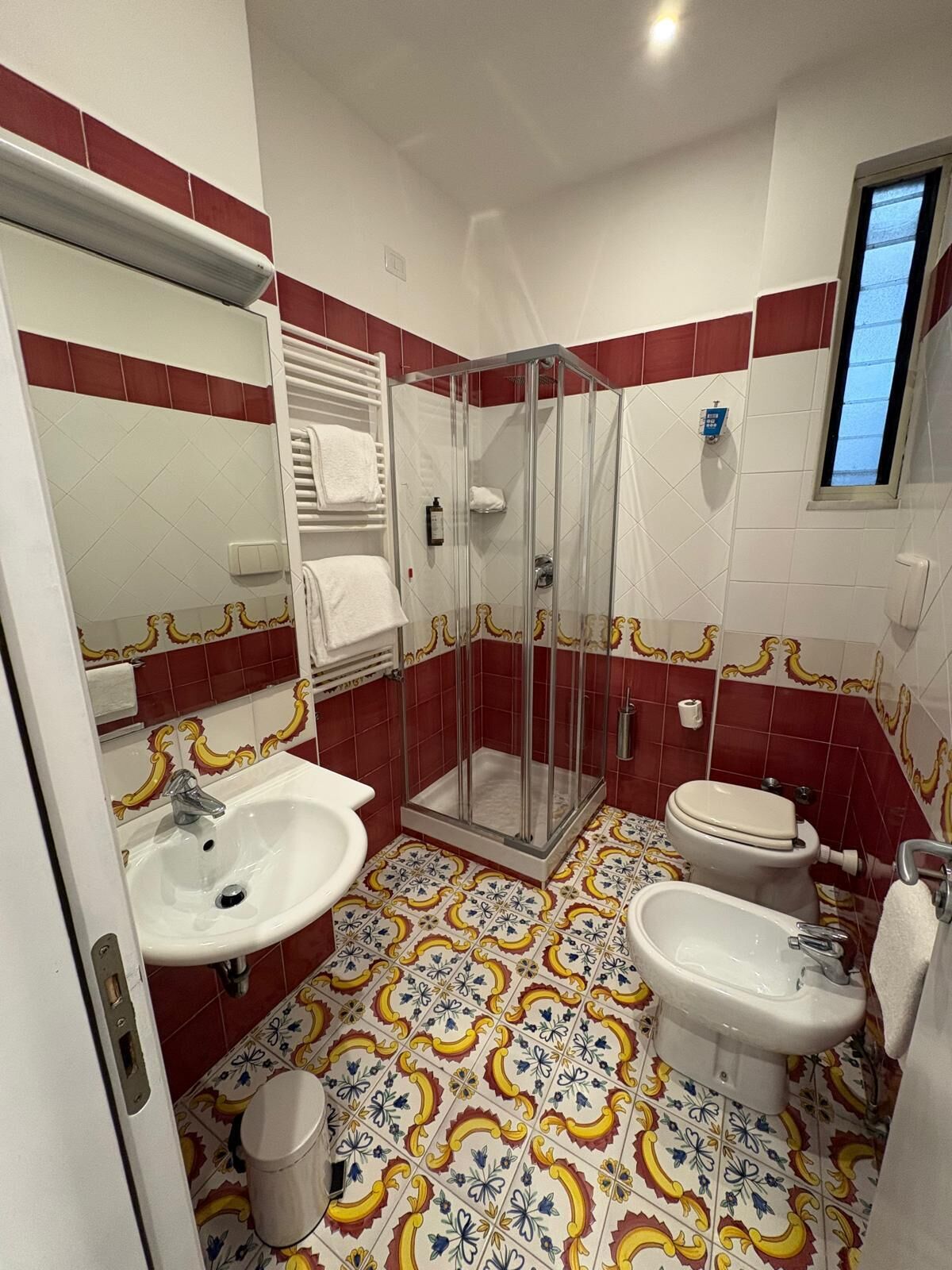 A bathroom with a shower, two sinks, a toilet, and a window.