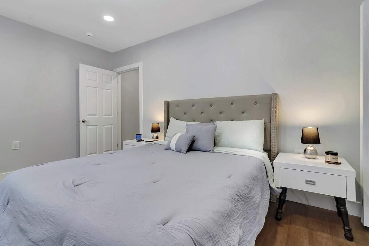 A bedroom with a large bed, two bedside tables with lamps, a door, and a white wall.