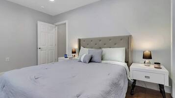 A bedroom with a large bed, two bedside tables with lamps, a door, and a white wall.