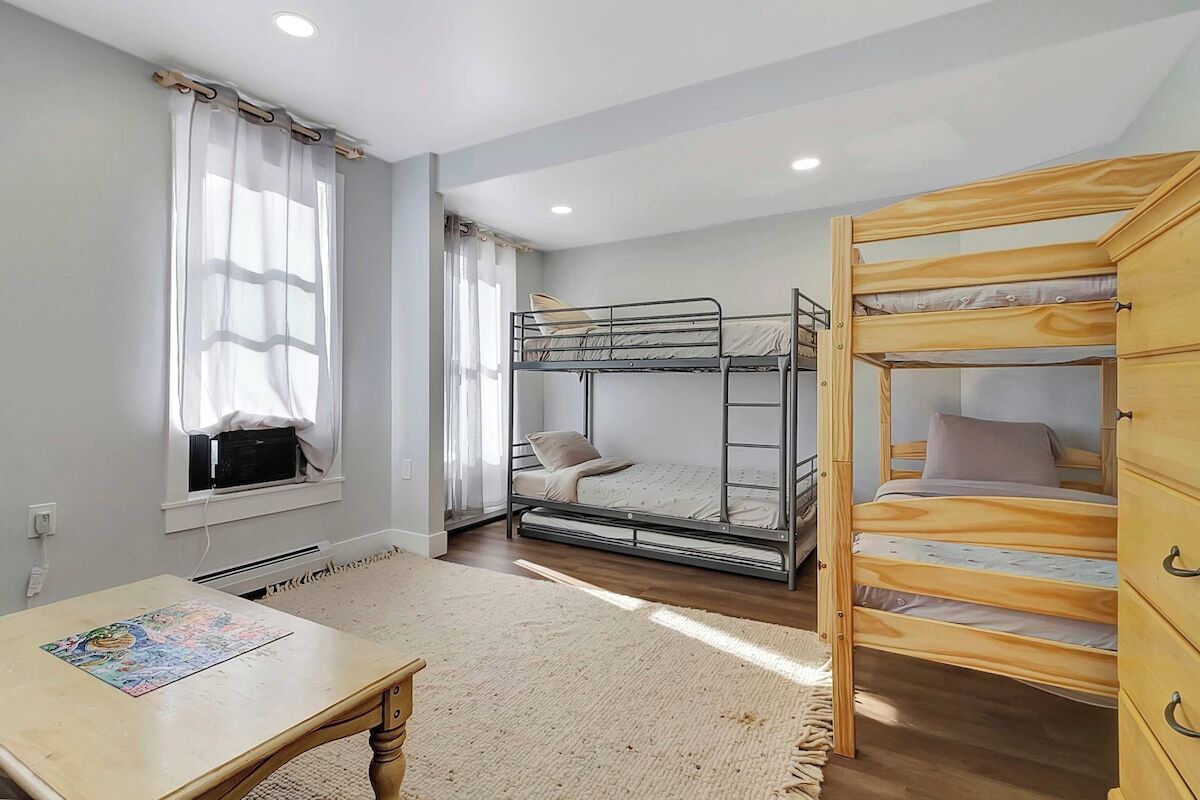 A room with bunk beds, a table with a puzzle, and a window with curtains.