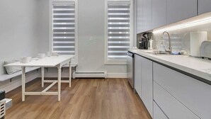 A compact kitchen with white cabinetry, a built-in oven, and a dining area with a white table and bench. - 4BR Home | Walk Downtown Rutland + Trails (Rutland)