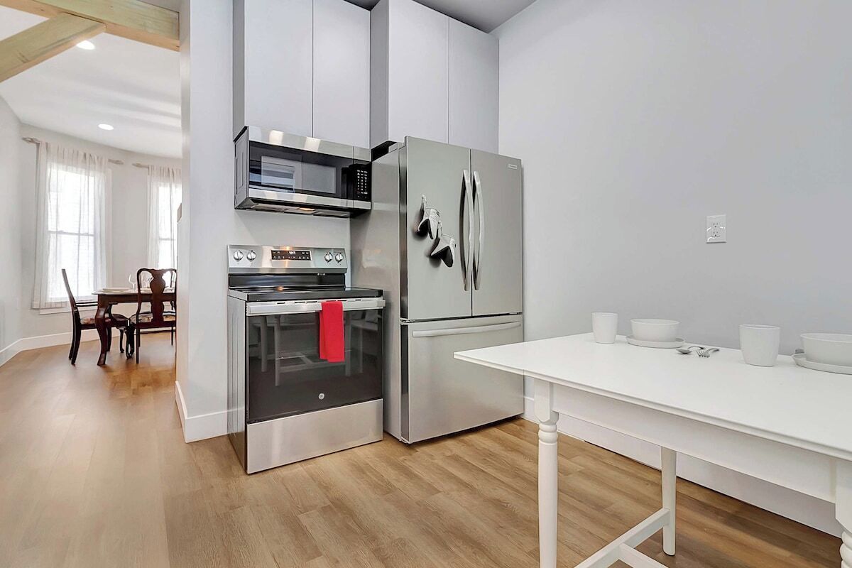 A modern kitchen with stainless steel appliances, a dining table, and a wooden floor.