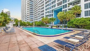 A hotel with a rooftop pool, lounge chairs, and palm trees.