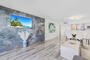 A modern hotel room with a marble wall, a flat-screen TV, a vase with white feathers, a dining area with white furniture, and a kitchen area. - Balcony & Bay View | Downtown | Gym | StayCozy (Miami)