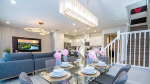 A modern dining area with a glass table, grey upholstered chairs, and a chandelier.