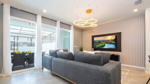 A living room with a grey sofa, a flat-screen TV, and a large window.