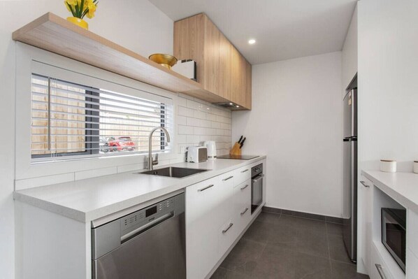 Una cocina moderna con armarios blancos, lavavajillas integrado, refrigerador de acero inoxidable y una ventana con persianas.