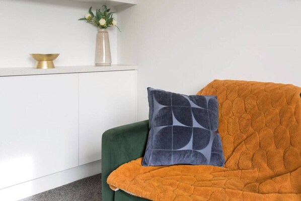 A green chair with an orange blanket and a patterned pillow.