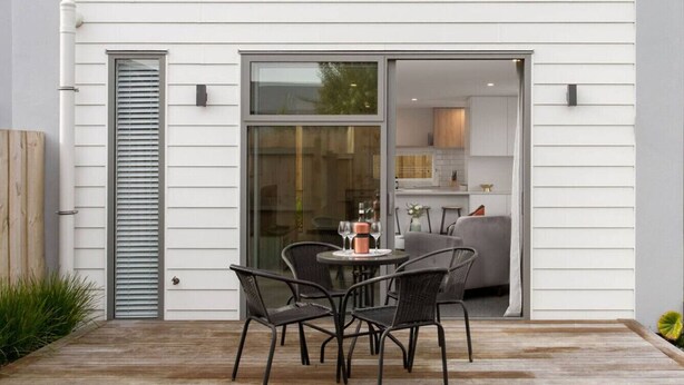 A patio with a table and chairs, a sliding glass door, and a view into a kitchen area.