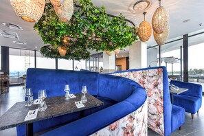 Ein modernes Restaurant mit einem blau gepolsterten Sitzbereich, einem Tisch mit Weingläsern und hängenden Gewebedeckenleuchten.