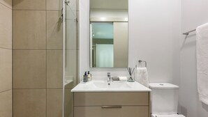 Une salle de bain moderne avec une douche à parois de verre, un lavabo blanc avec un miroir au-dessus, et des toilettes avec une serviette accrochée au mur.