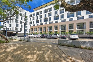 Ein mehrstöckiges Gebäude mit modernem Design, das einen Parkbereich mit mehreren Autos und einen überdachten Gang zeigt.