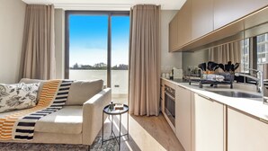 Un salon moderne avec un canapé, une petite table d’appoint et une vue sur la ville grâce à de grandes fenêtres.