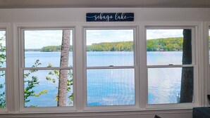 Huoneessa on suuri ikkuna, josta avautuu näkymä Sebago-järvelle. Ikkunan ympärillä on valkoiset koristelistat, ja sen yläpuolella on kyltti, jossa lukee ”Sebago Lake”.