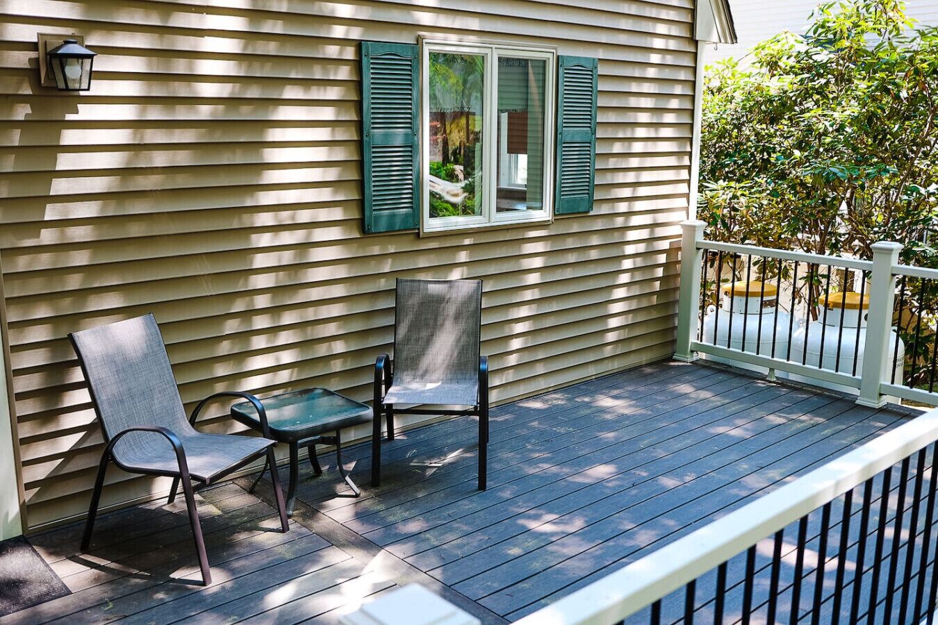 A covered porch with two chairs and a table, a window with shutters, and a white railing.