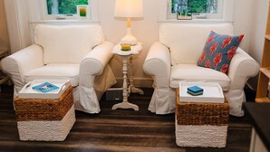Une pièce chaleureuse avec deux fauteuils blancs, une petite table avec une lampe et des paniers en osier posés sur le sol.