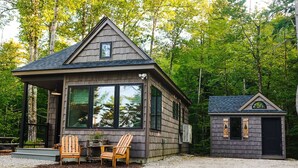 Une cabane avec une véranda, deux chaises en bois et un petit abri de jardin.