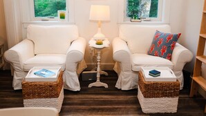 Une pièce chaleureuse avec deux canapés blancs, une petite table avec une lampe et une vue sur la verdure par les fenêtres.