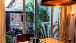 Un espace repas avec une table en bois, des chaises et une vue sur un bâtiment en briques et la verdure environnante.