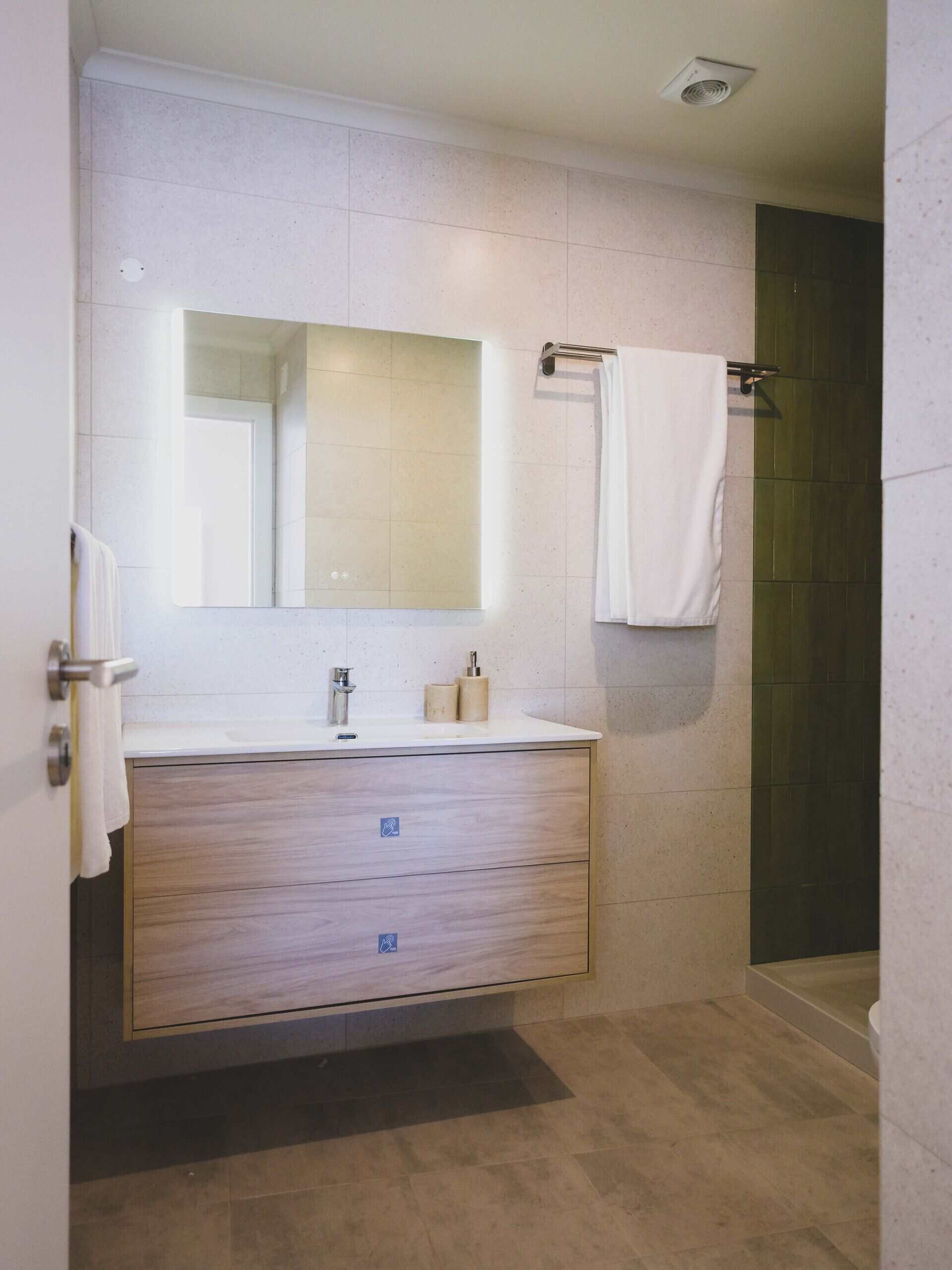 A modern bathroom with a wooden vanity, a large mirror, a towel rack, and a shower area.