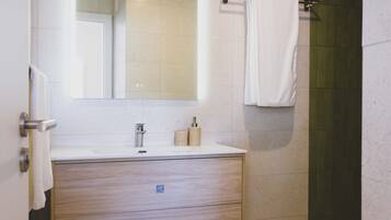 A modern bathroom with a wooden vanity, a large mirror, a towel rack, and a shower area.