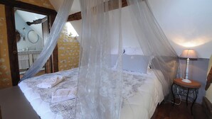 Une chambre à coucher avec un lit à baldaquin, une lampe de chevet et une salle de bain visible à travers une porte ouverte.