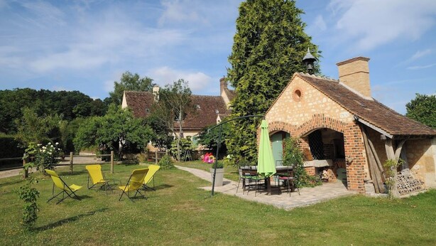 Un bâtiment rustique avec une cheminée en briques, entouré d’une pelouse verdoyante et de chaises jaunes.