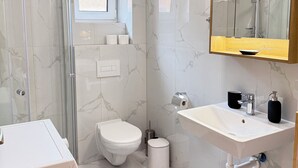 A modern bathroom with a glass shower enclosure, a toilet, a sink with a mirror, and a window above the toilet. - Riverside Apartment 11 (Hlavní město Praha)