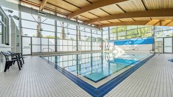A swimming pool with a tiled floor and a wooden ceiling, surrounded by large windows.