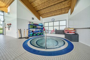 Una piscina con suelo de baldosas azules y blancas, rodeada por un techo de madera y paredes blancas.