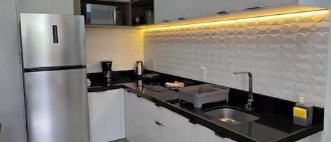 Une cuisine moderne avec des meubles blancs, un réfrigérateur en acier inoxydable, un plan de travail noir et un pare-feu en carrelage.