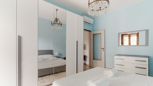 Une chambre à coucher avec un grand lit, une armoire, un miroir et un lustre.